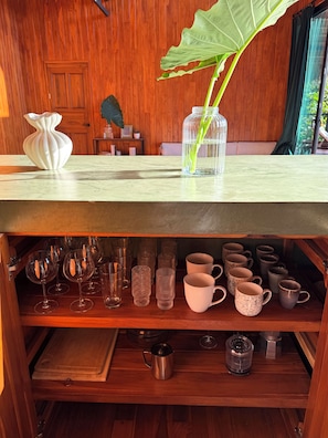 Ein Holzinnenraum mit einem Tisch, auf dem eine Vase und eine Pflanze stehen, einem Regal mit verschiedenen Gläsern und einem Holzkabinett.