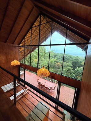 Ein Zimmer mit hohen Decken, großen Fenstern, einer Holzterrasse und einem Essbereich.