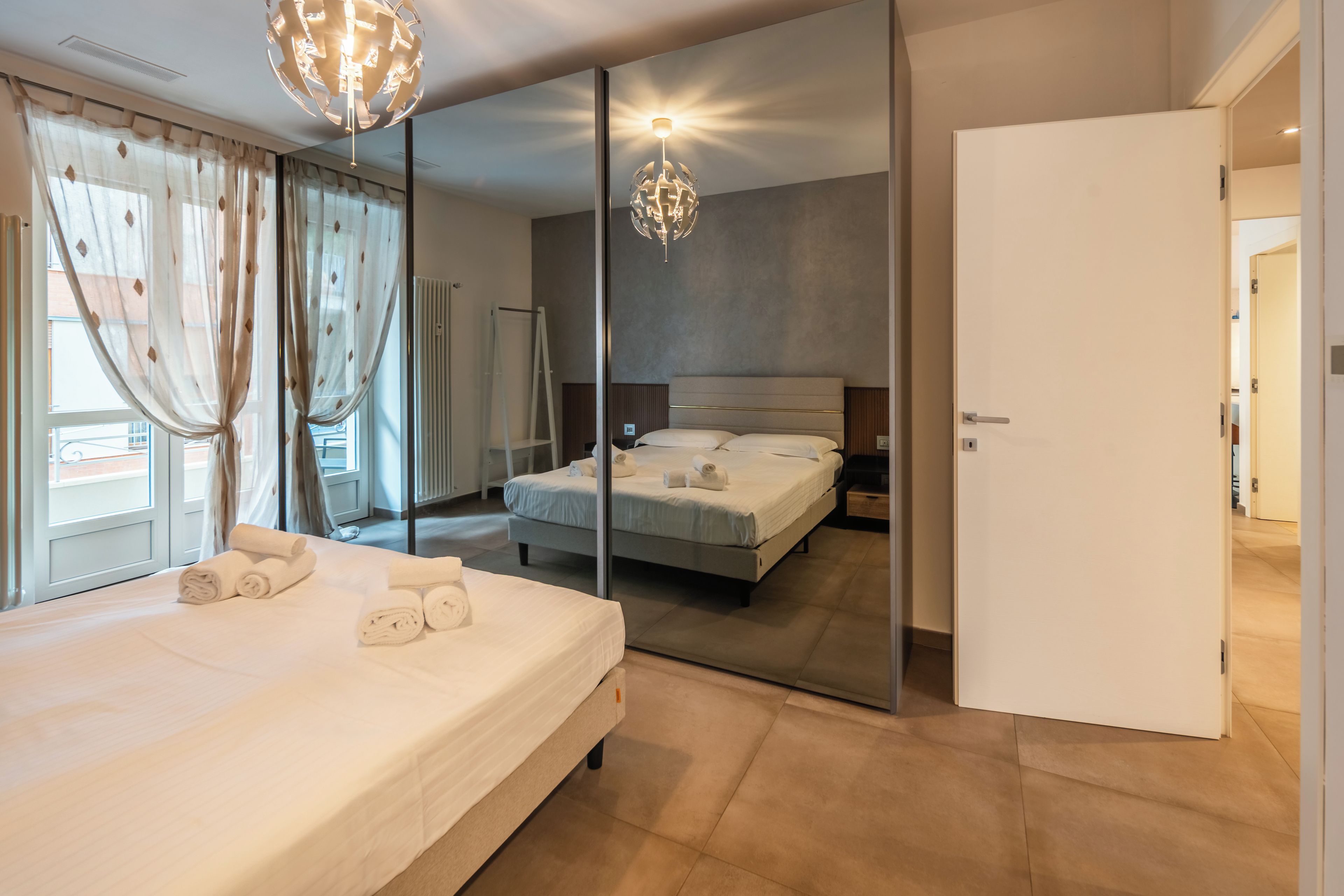 Quarto moderno com um espelho grande, uma cama e toalhas dobradas, com vista para o quarto vizinho.