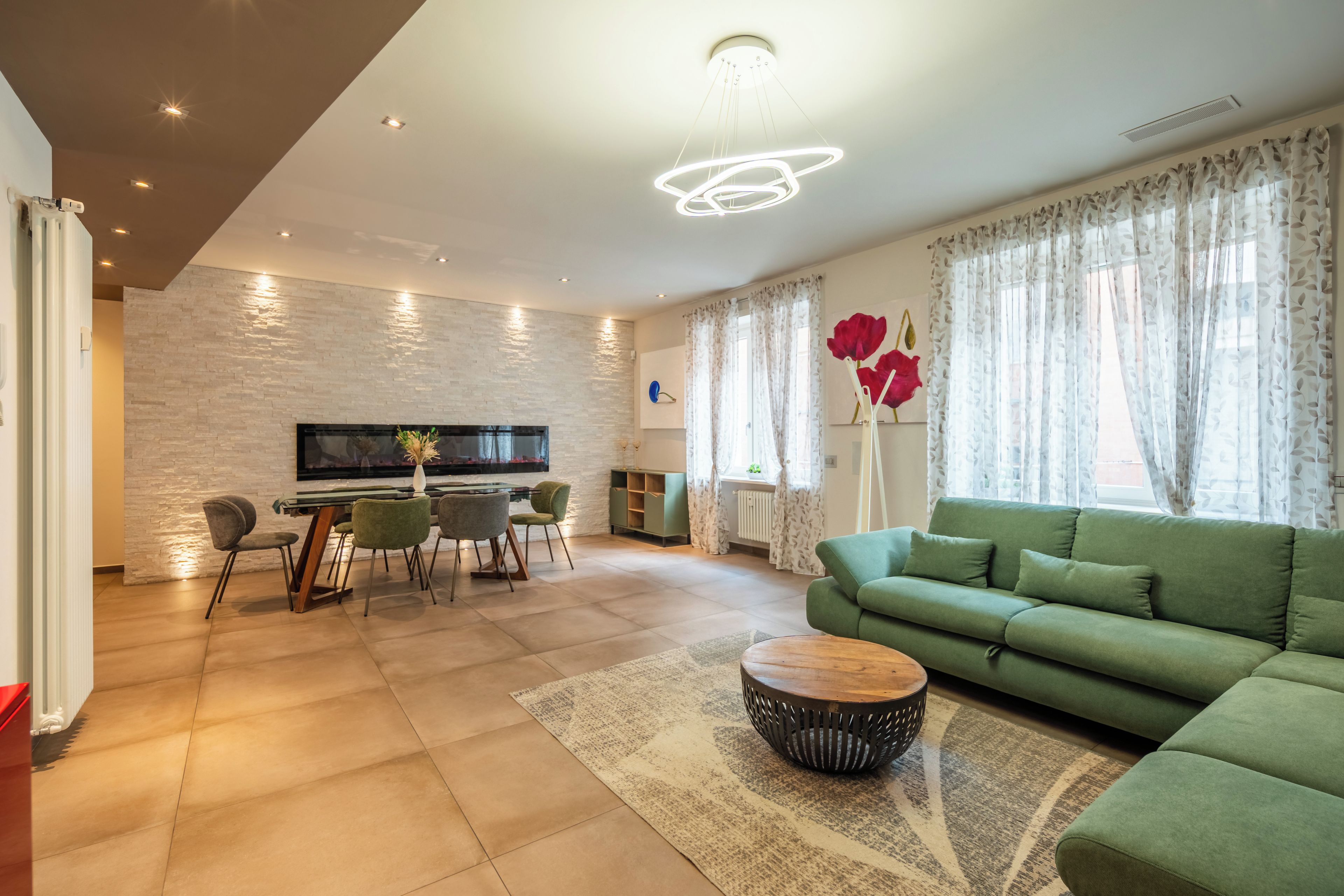 Una sala de estar moderna con un sofá verde, una mesa de comedor con sillas, un televisor de pantalla plana montado en una pared de piedra y una chimenea.