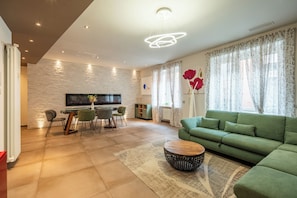 Una sala de estar moderna con un sofá verde, una mesa de comedor con sillas, un televisor de pantalla plana montado en una pared de piedra y una chimenea.