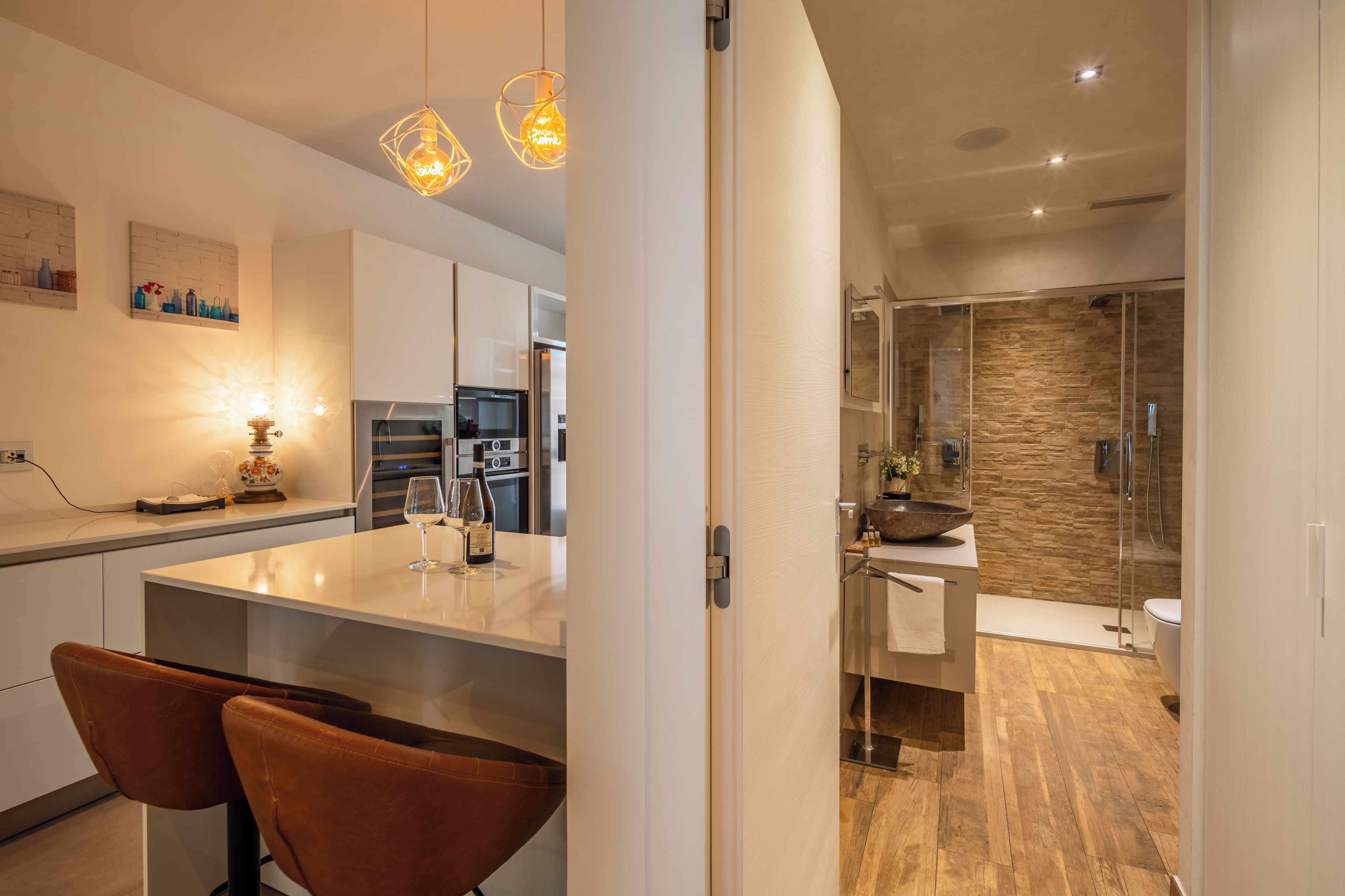 Una cocina moderna con electrodomésticos de acero inoxidable, un comedor con dos sillas de cuero y una zona de ducha con cerramiento de vidrio.