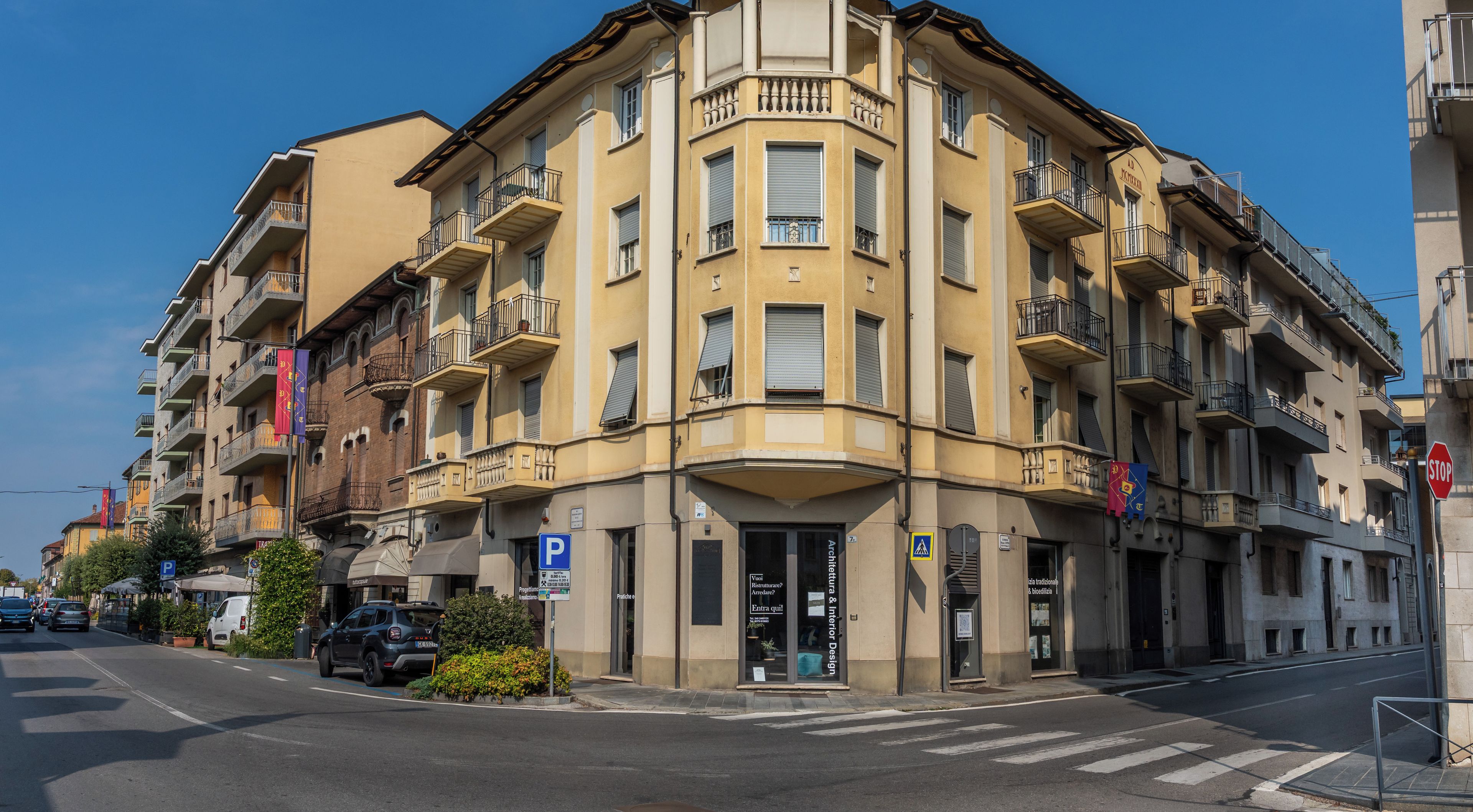 Un edificio de varios pisos con entrada en esquina, un letrero de estacionamiento visible y una señal de parada.