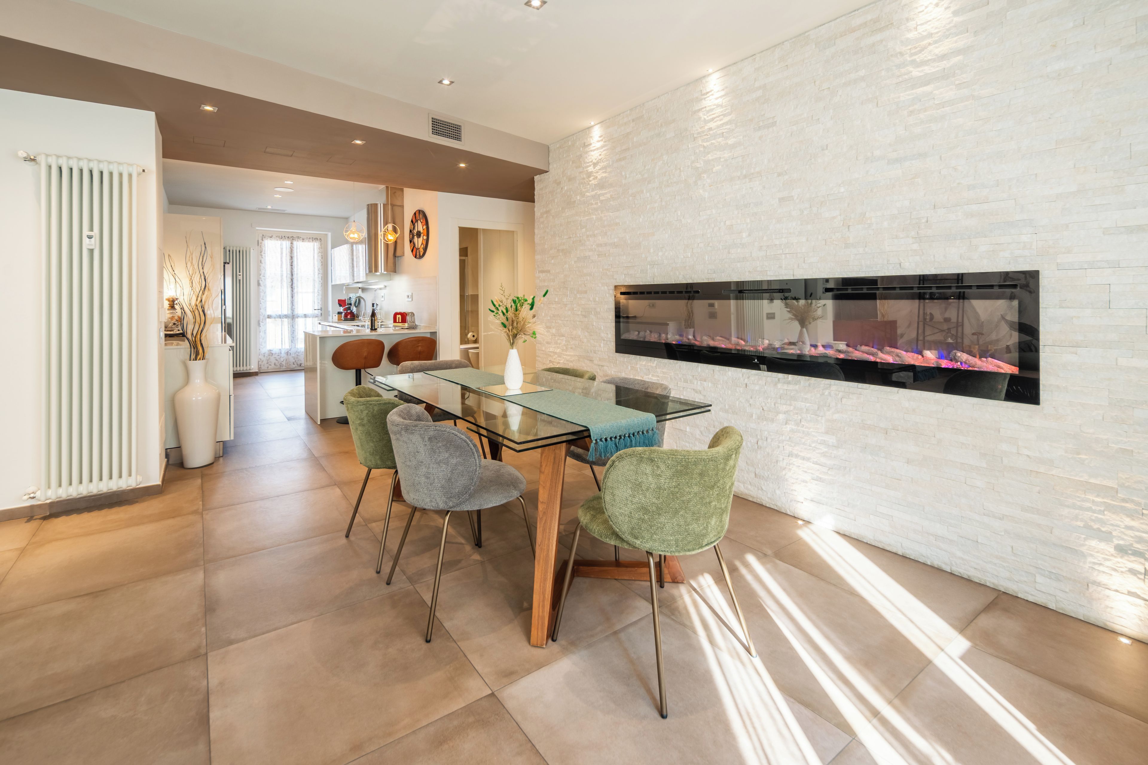 Una cocina moderna con comedor, que incluye una mesa de vidrio, sillas tapizadas en verde y una chimenea empotrada.