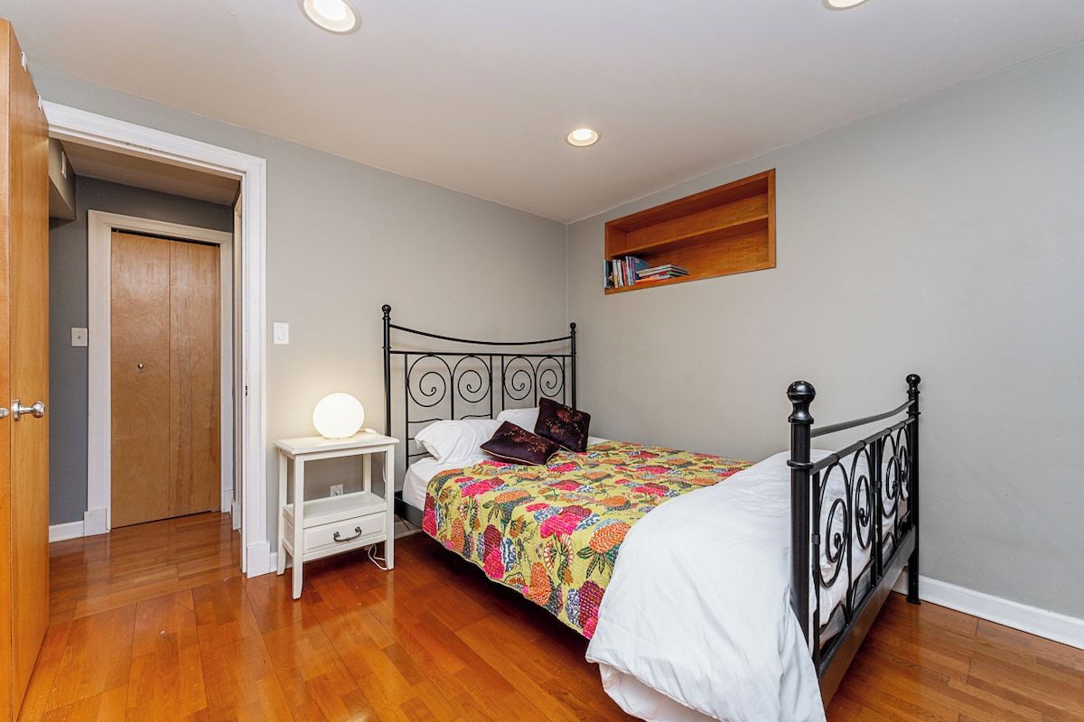A bedroom with a bed, bedside table, and a shelf with books.