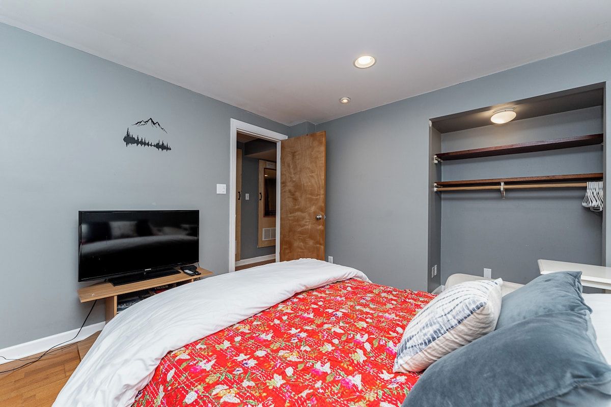A bedroom with a bed, a television on a stand, a wardrobe, and a door leading to another room.