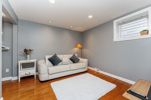 A modern living room with a white sofa, a small side table, a lamp, and a window with a plant. - Garden suite by DSOUZA (Vancouver)