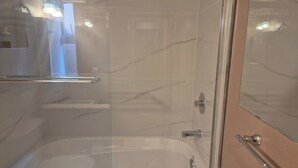 A bathroom with a glass shower enclosure, a bathtub, and a mirror. - Garden suite by DSOUZA (Vancouver)