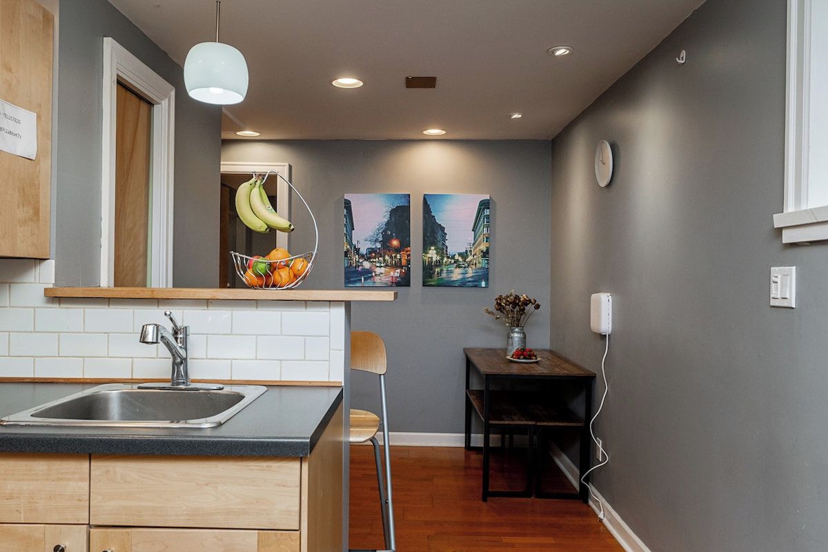 A modern kitchen with a sink, a fruit basket, and two paintings on the wall.