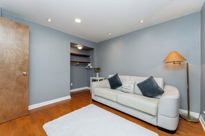 A room with a white sofa, a floor lamp, and a wooden door. - Garden suite by DSOUZA (Vancouver)