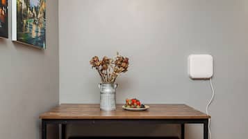 Ein Tisch mit einer Vase getrockneter Blumen, einer kleinen Teller mit Essen, einer Steckdose und einem Bild an der Wand.