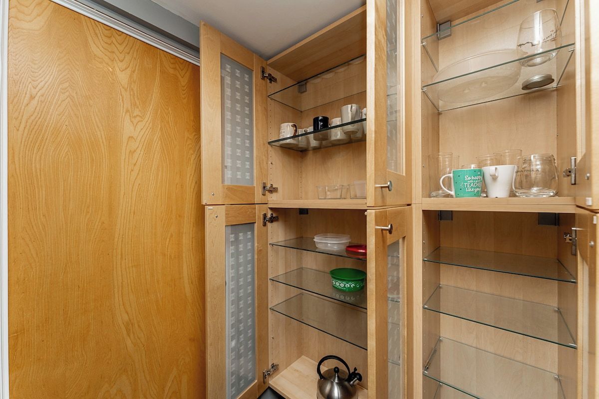 A wooden cabinet with multiple shelves, some containing glassware and a kettle.