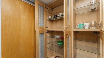 A wooden cabinet with multiple shelves, some containing glassware and a kettle.