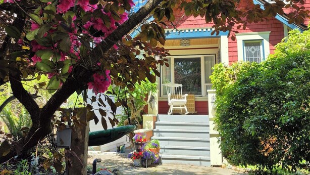 A house with a porch, a chair, and a garden with pink flowers. - Garden suite by DSOUZA (Vancouver)
