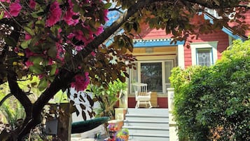 Ein Haus mit Veranda, einem Stuhl und einem Garten mit rosa Blumen.