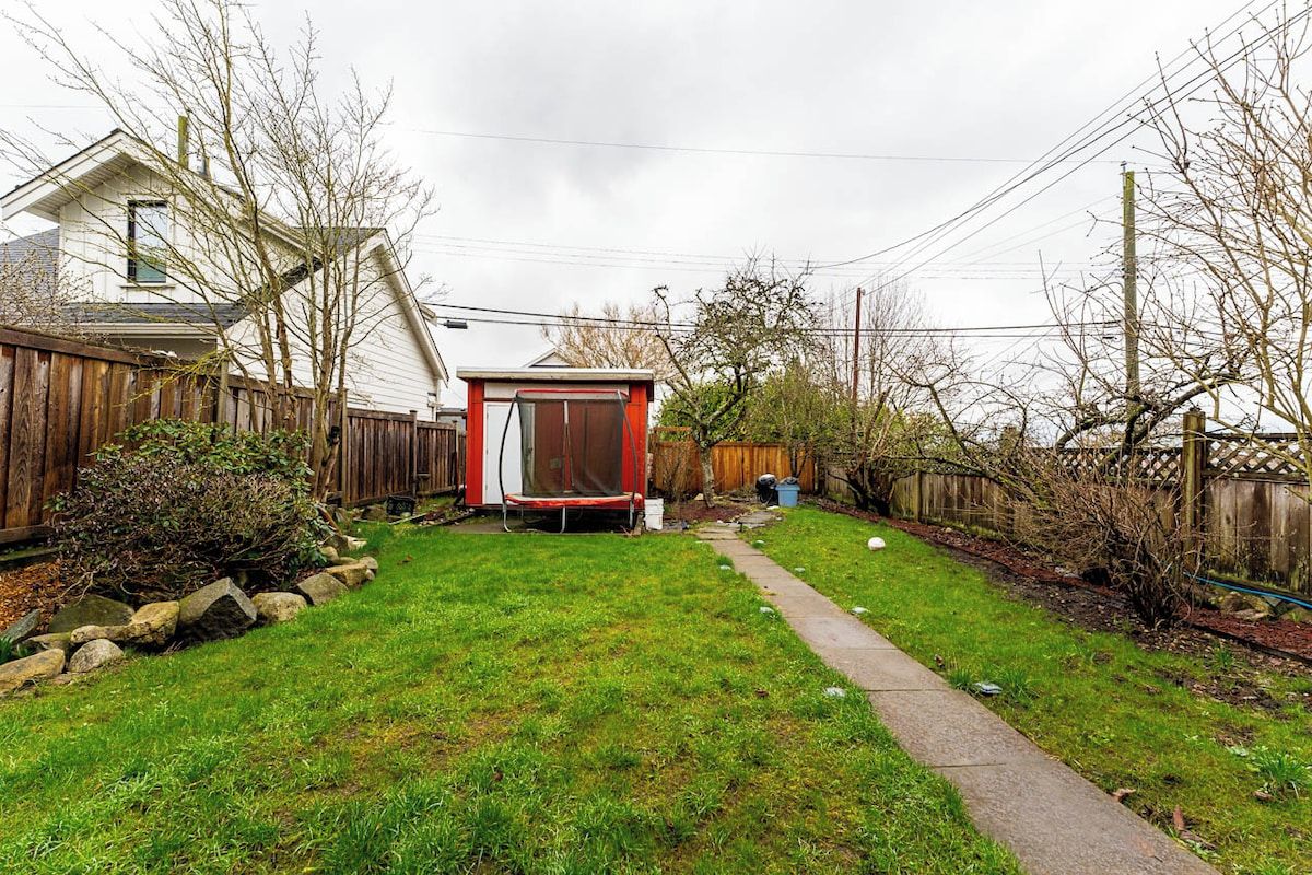 Ein Garten mit Trampolin, Holzzaun und einem Weg zum Haus.