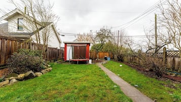 Ein Garten mit Trampolin, Holzzaun und einem Weg zum Haus.