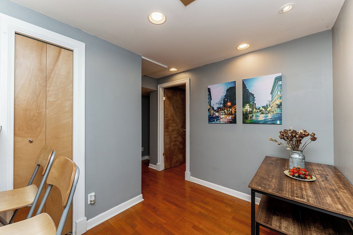 A hallway with wooden flooring, a dining table with a vase of dried flowers, and two framed pictures on the wall.