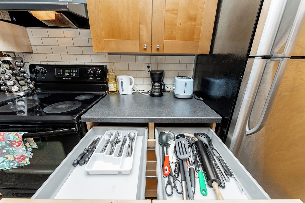 A kitchen with a stove, coffee maker, toaster, and a drawer with utensils.