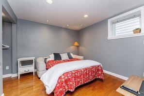 A bedroom with a bed, bedside table, lamp, and a window with blinds.