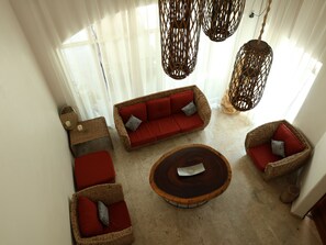Een kamer met een zithoek, een rond bijzettafeltje en rieten stoelen.