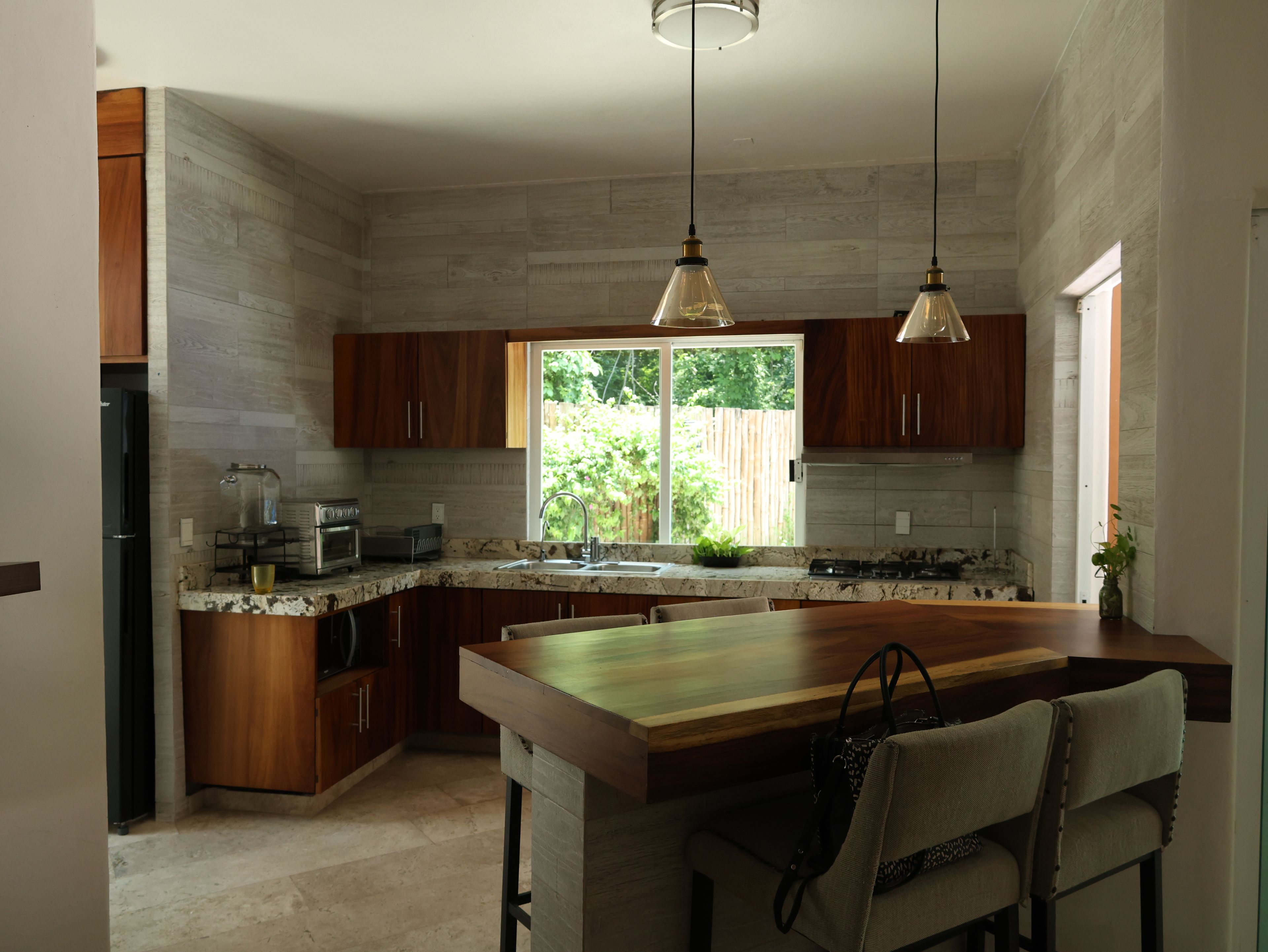 A modern kitchen with a large island, wooden cabinets, and pendant lighting.