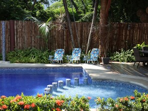 A swimming pool with three lounge chairs and a table, surrounded by a bamboo fence and tropical plants. - Just 5 minutes from the beach! An ideal home for families or groups. (Ixtapa Zihuatanejo)
