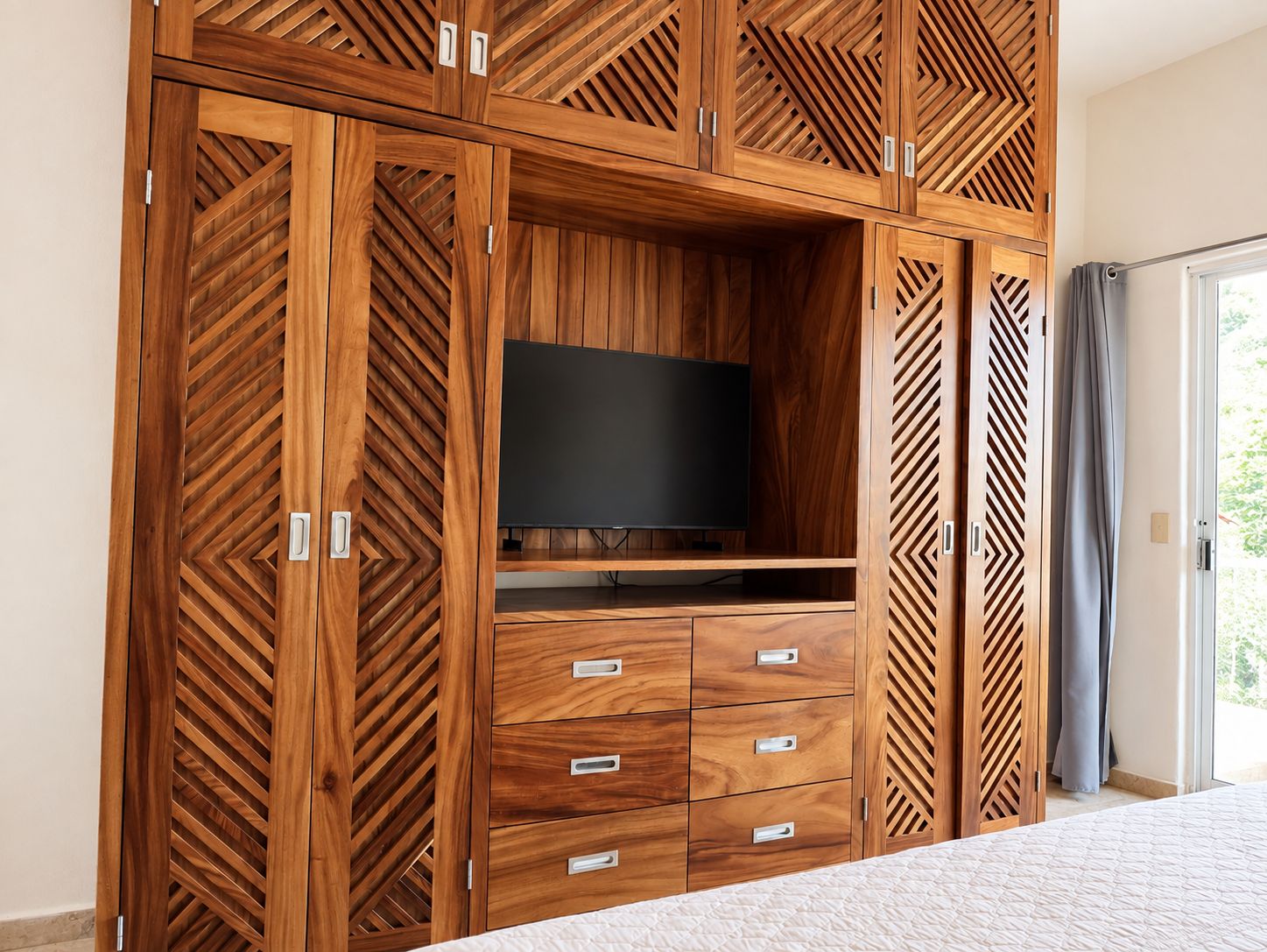 Une chambre dotée d’une grande armoire en bois, d’un téléviseur à écran plat et d’un lit recouvert d’une courtepointe matelassée.