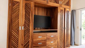 Ein Schlafzimmer mit großem Holzkoffer, einem Flachbildfernseher und einem Bett mit gesteppter Bettdecke.
