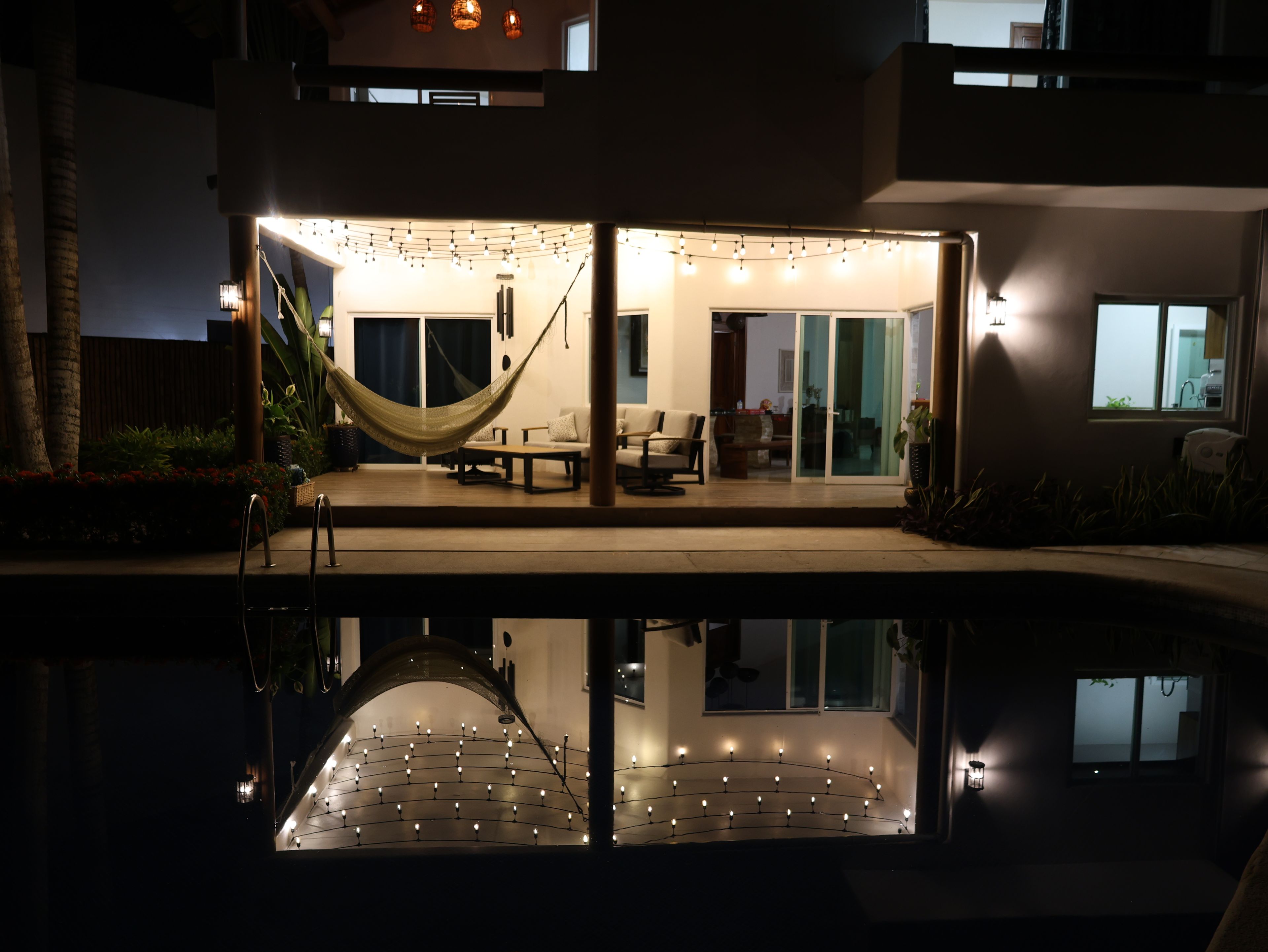 Un espace de détente extérieur moderne, doté d’un hamac, de sièges et de guirlandes lumineuses.