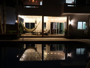 A modern outdoor lounge area with a hammock, seating, and string lights. - Just 5 minutes from the beach! An ideal home for families or groups. (Ixtapa Zihuatanejo)