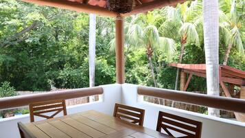 Ein Holztisch mit Stühlen steht unter einer Pergola mit Blick auf üppiges Grün.
