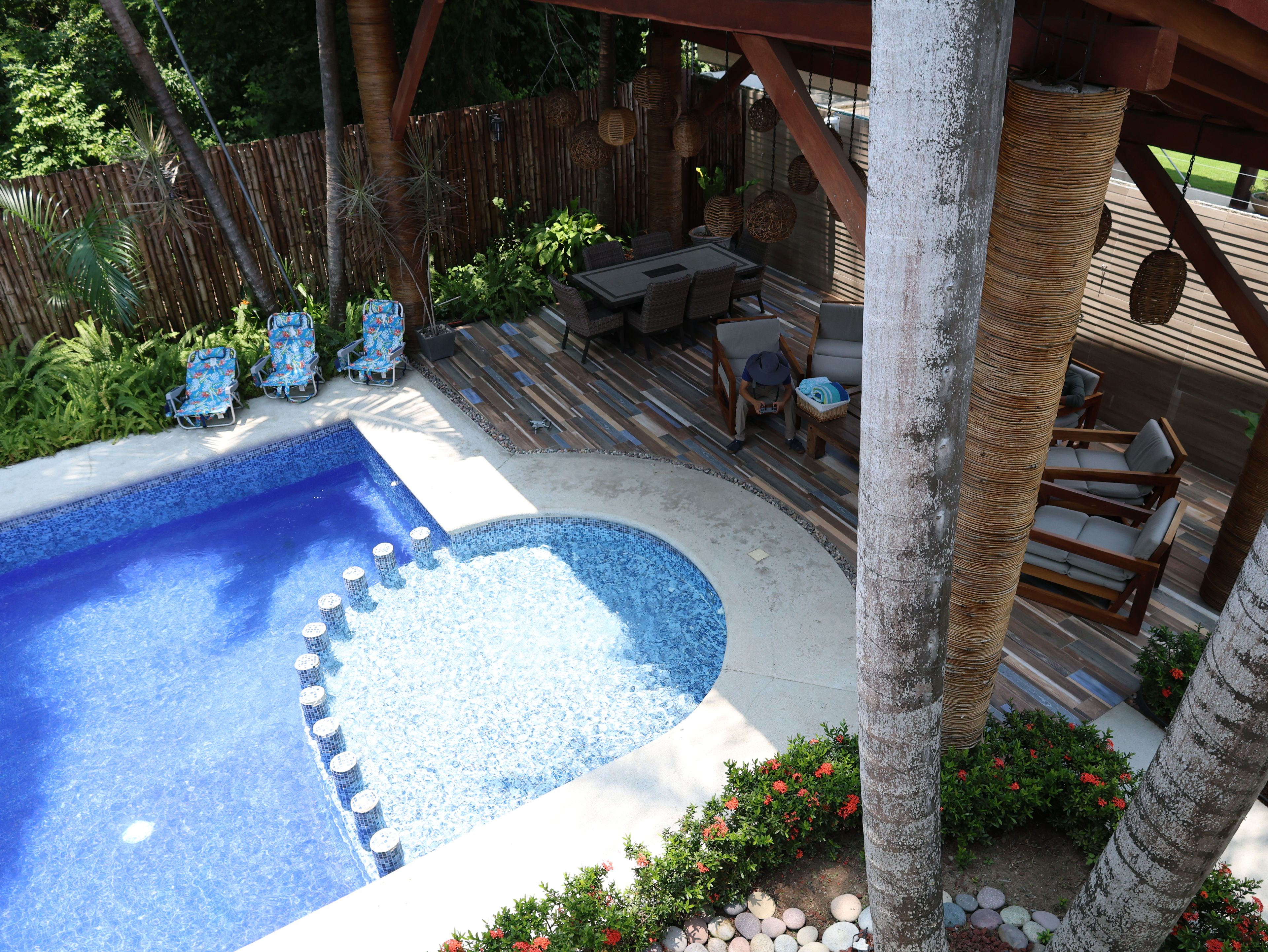 A backyard with a swimming pool, lounge chairs, a wooden deck, and a covered patio area.