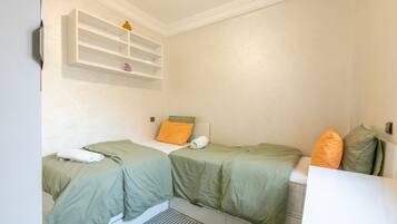 A room with two beds, a shelf with decorative items, and a white wall.