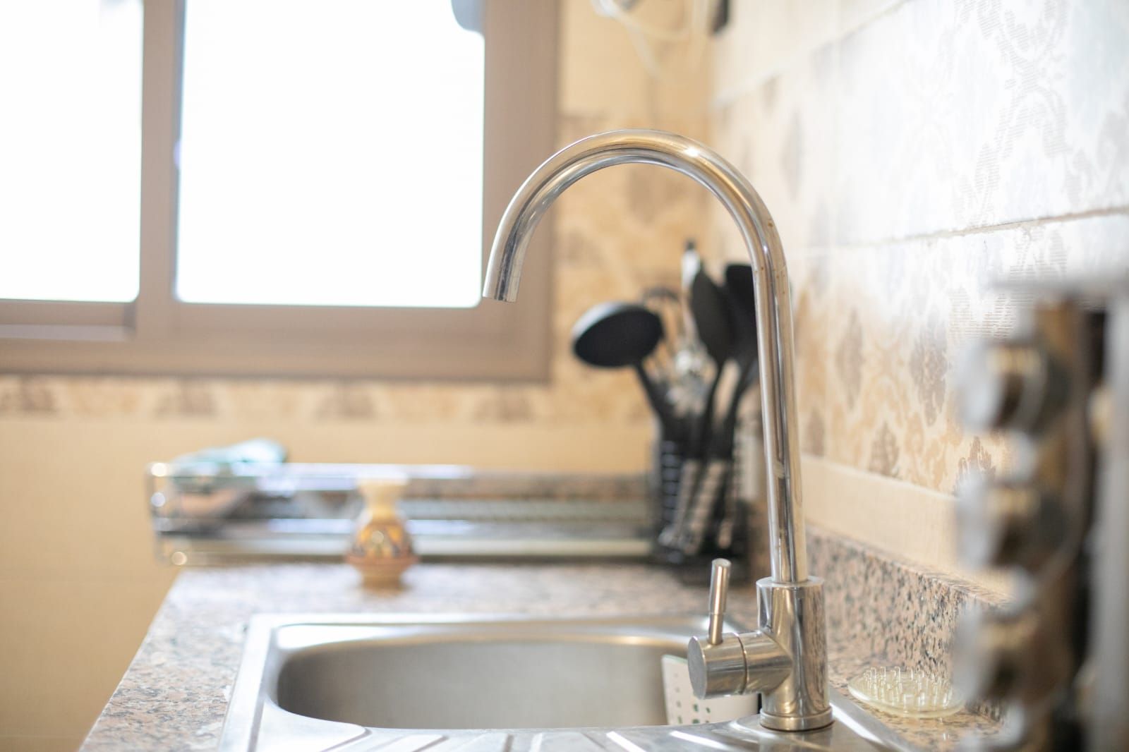A kitchen with a stainless steel sink, a window above the sink, and a backsplash with a patterned tile design.
