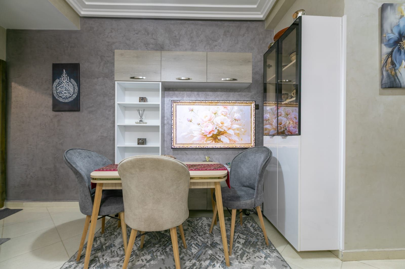 A dining area with a table and chairs, a cabinet with shelves, and a refrigerator.