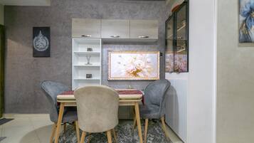 A dining area with a table and chairs, a cabinet with shelves, and a refrigerator.