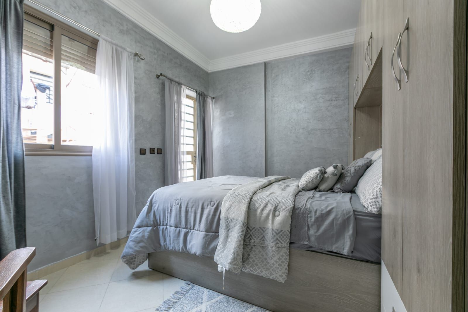 A bedroom with a bed, curtains, a window, and a wooden wardrobe.