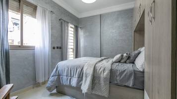 A bedroom with a bed, curtains, a window, and a wooden wardrobe.