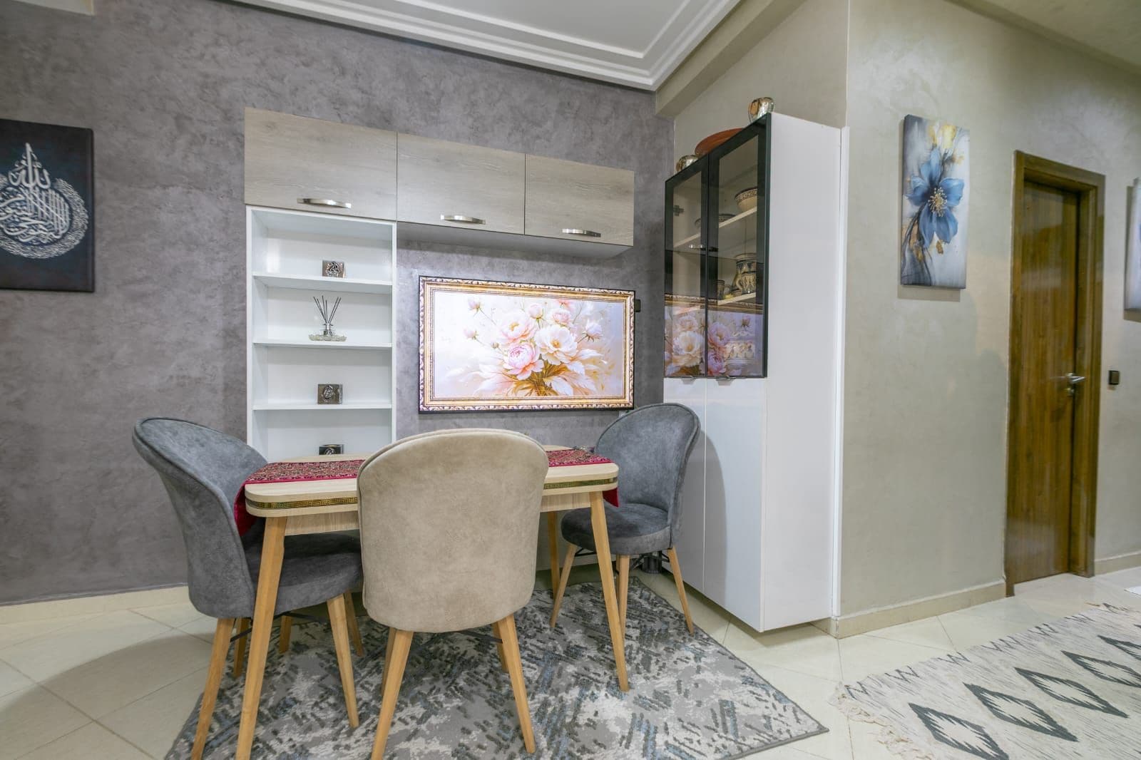 Ein Essbereich mit Tisch und Stühlen, eine Kommode mit Dekoration und ein gerahmtes Blumenbild an der Wand.