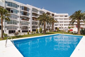 A hotel with a swimming pool, palm trees, and a white building with balconies. - Studio in Nerja Near Carabeillo Beach (Nerja)