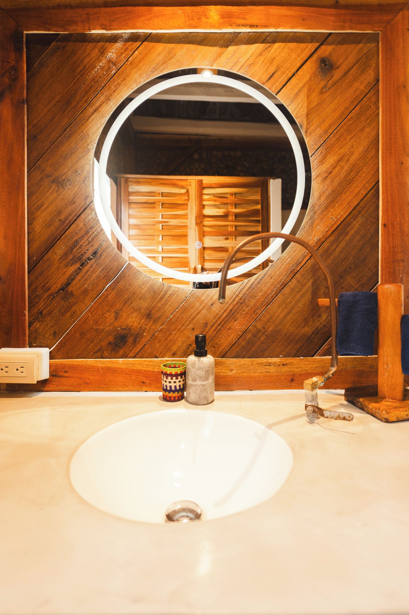 A bathroom with a wooden wall, a round mirror, a white sink, and a towel rack.