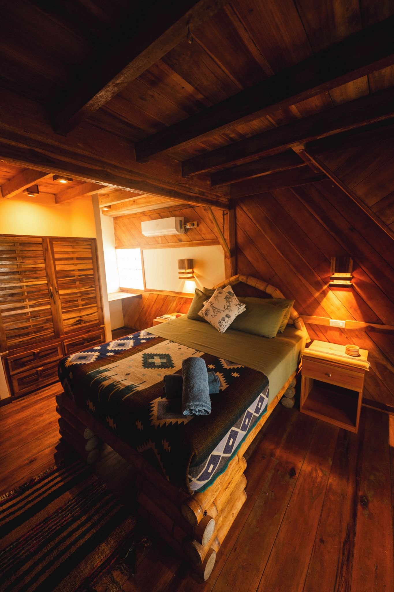 Une chambre mansardée chaleureuse, avec un lit, une table de chevet et une armoire en bois.