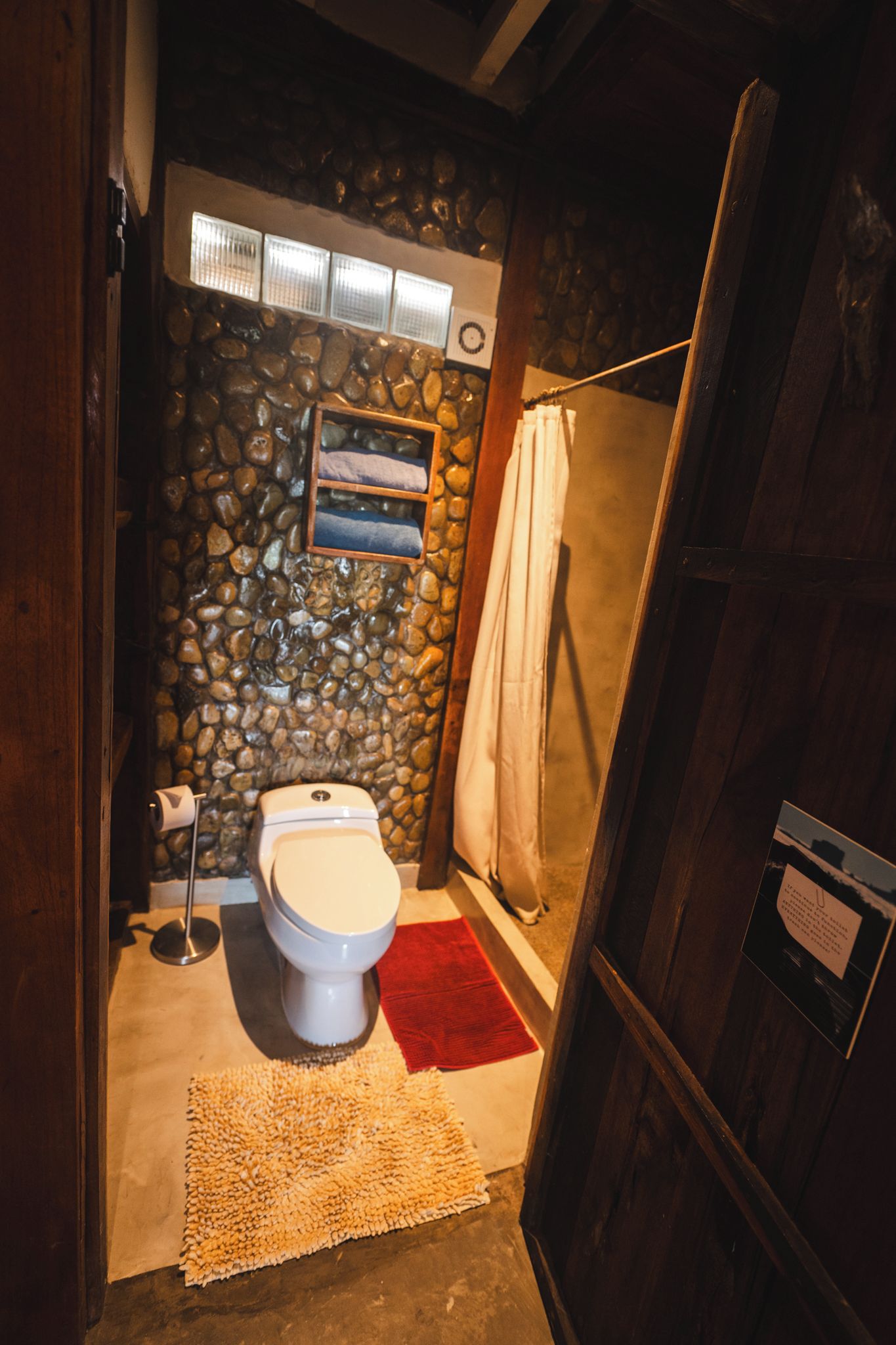 Un baño con pared de piedra, un inodoro, una ducha y una puerta de madera.