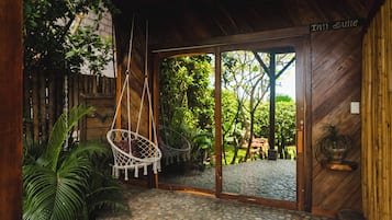 Een houten interieur met een hangstoel, een betegelde inkomhal en uitzicht op een buitenplaats.