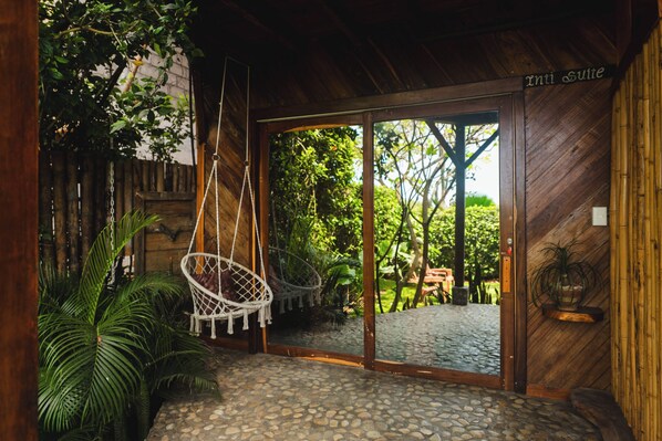 A wooden interior with a hanging chair, a stone-tiled entrance, and a view of an outdoor garden.