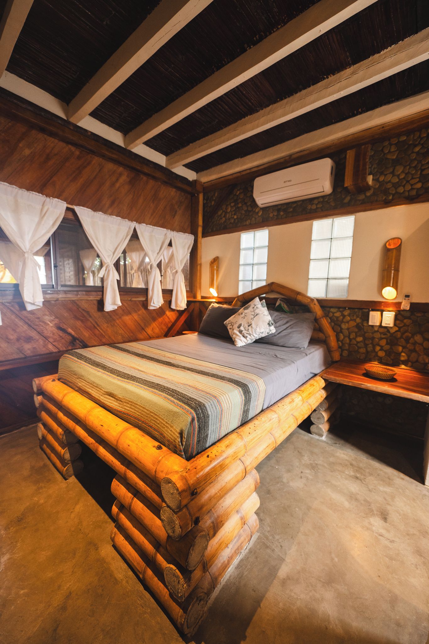 Una cama de madera rústica con cabecera, una pared de piedra y una ventana con vistas.