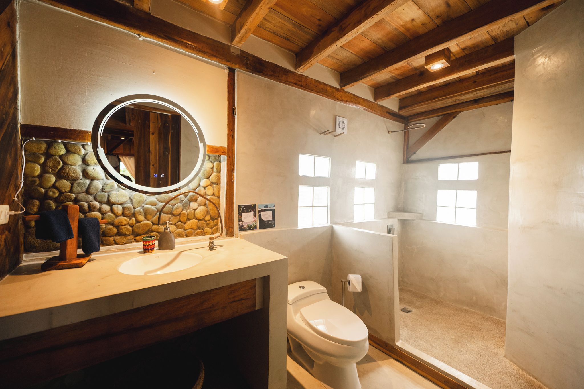 A bathroom with a stone wall, a round mirror, a sink, a toilet, and a shower area.