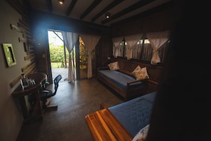 Un dormitorio acogedor con cama, una silla y una mesita. Hay una ventana con cortinas y vistas al exterior con vegetación.