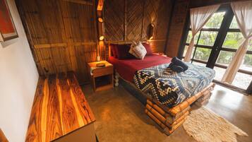 A room with a bed, a nightstand, a wooden bench, and a window with curtains.